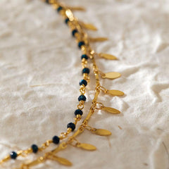 Beach layered retro copper plating 18K real gold anklet with black beads and gold charms on textured fabric background