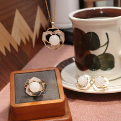 Natural Hetian white jade necklace ring and earrings set with gold floral design on brown surface next to teacup
