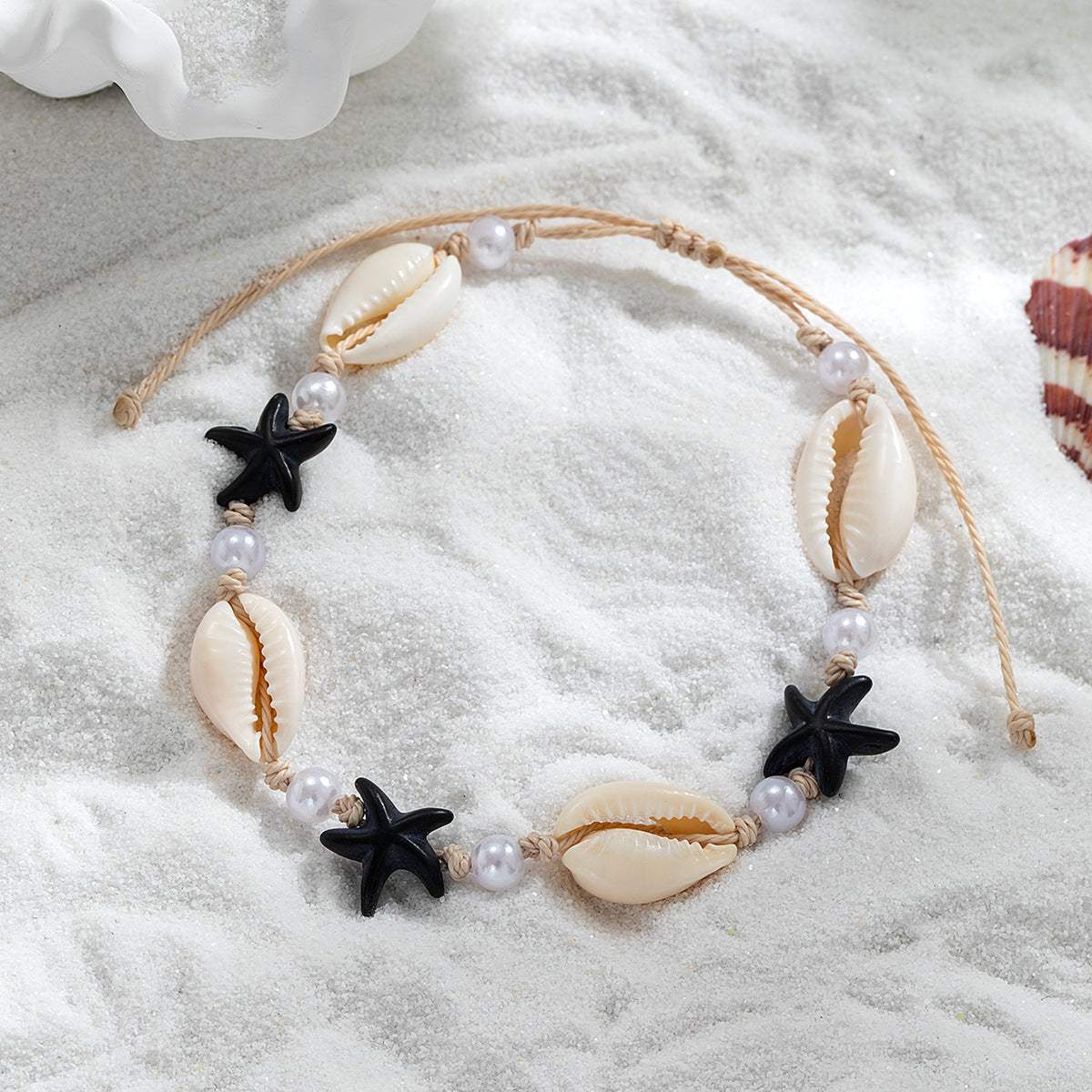 Adjustable starfish shell anklet with pearls on white sand background