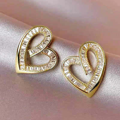 Pair of hollowed heart shape yellow gold ear studs with inlaid zircon stones on satin background
