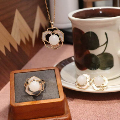 Natural Hetian white jade necklace ring and earrings set with gold floral design on brown surface next to teacup
